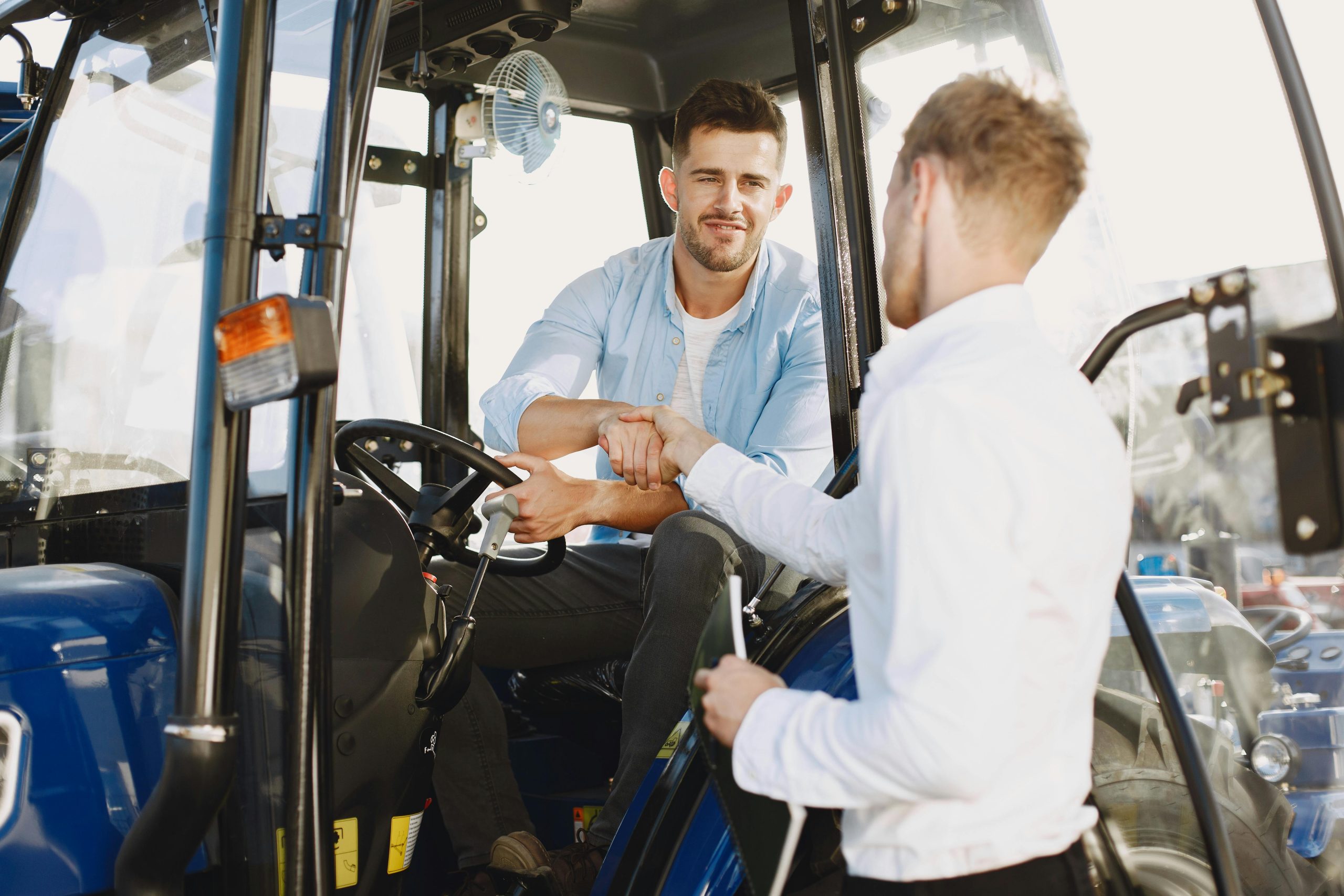 Two adults finalizing a business transaction with a handshake in a tractor.
